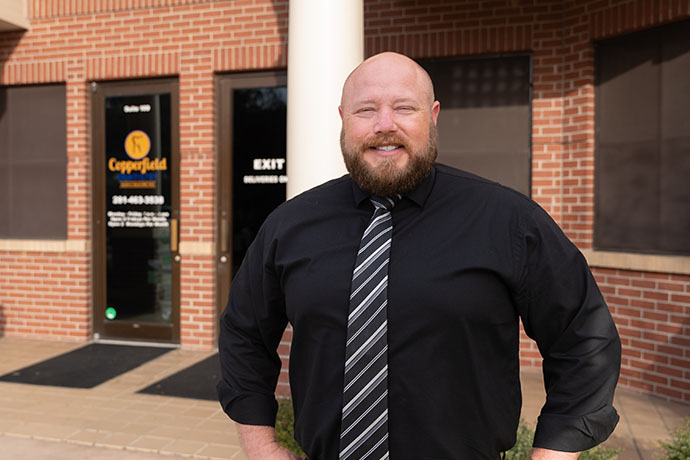 Dr. Jacob A. Burch smiles in front of the entrance of Copperfield Dentistry in Houston, TX